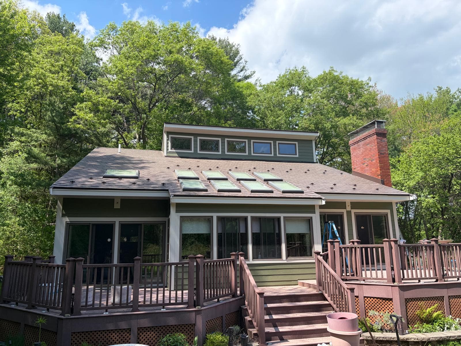 Rear of Carlisle MA home with James Hardie green siding, skylights, brick chimney, and deck surrounded by trees