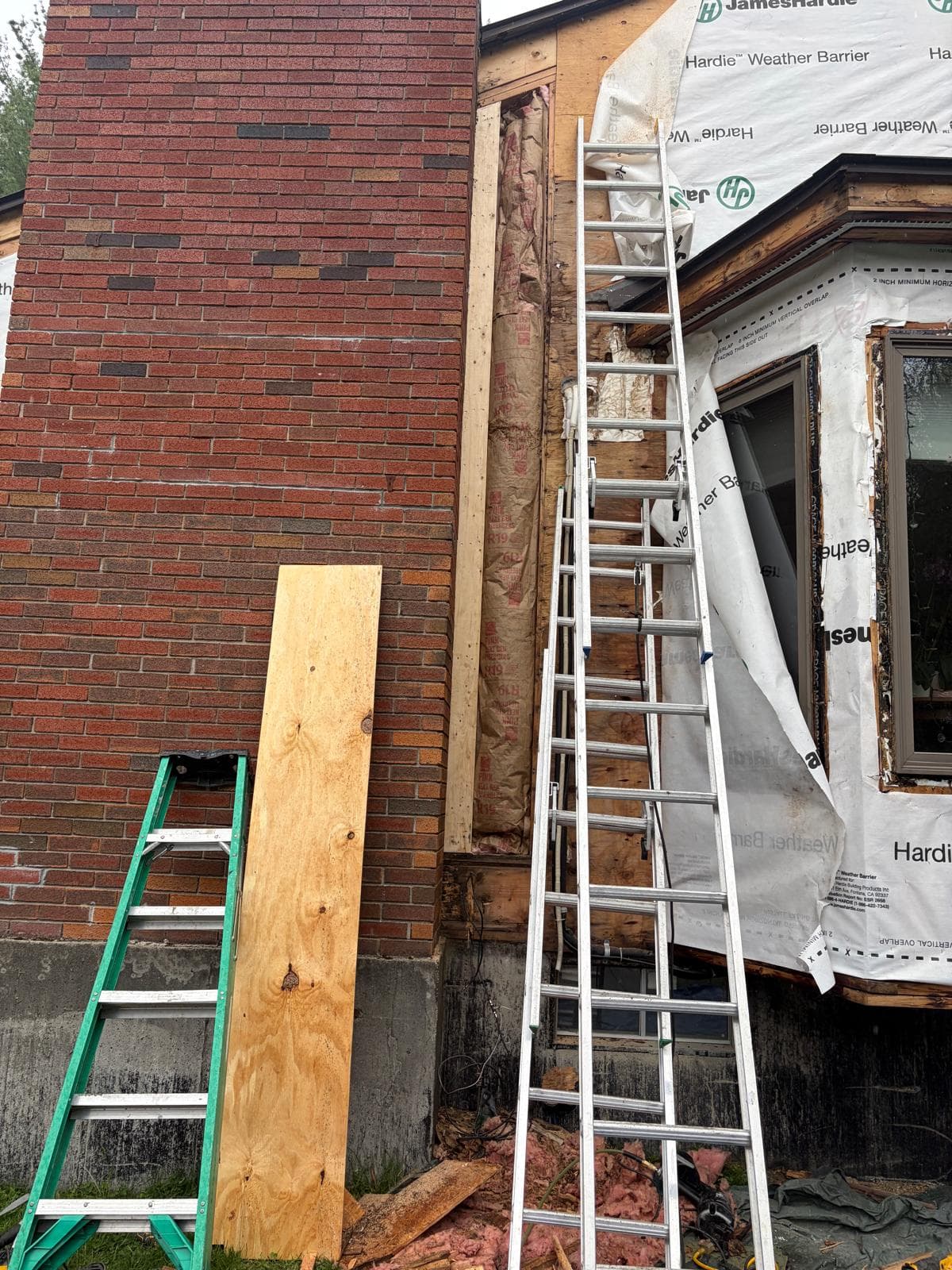 Brick chimney corner with raw plywood adjacent during siding removal at Carlisle MA Hardie project