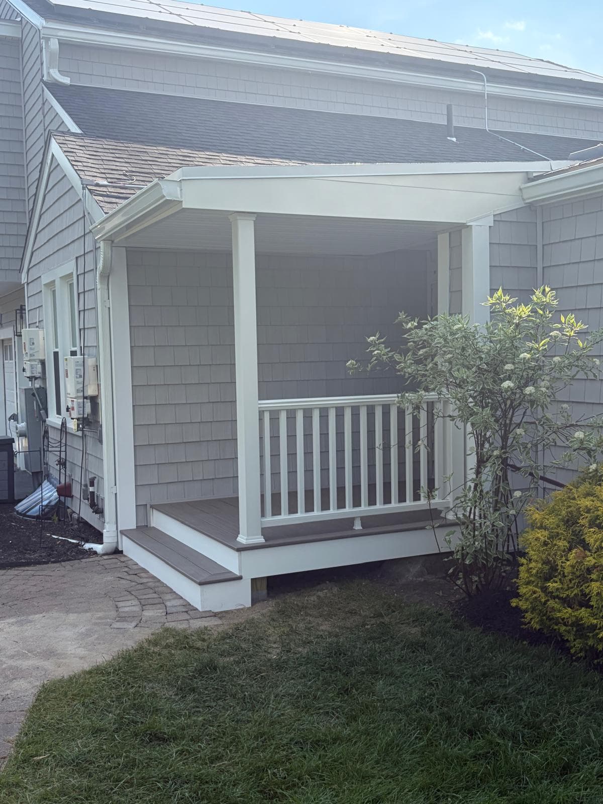Close detail of finished Webster MA porch interior showing composite deck flooring, white railing, and cedar shake walls