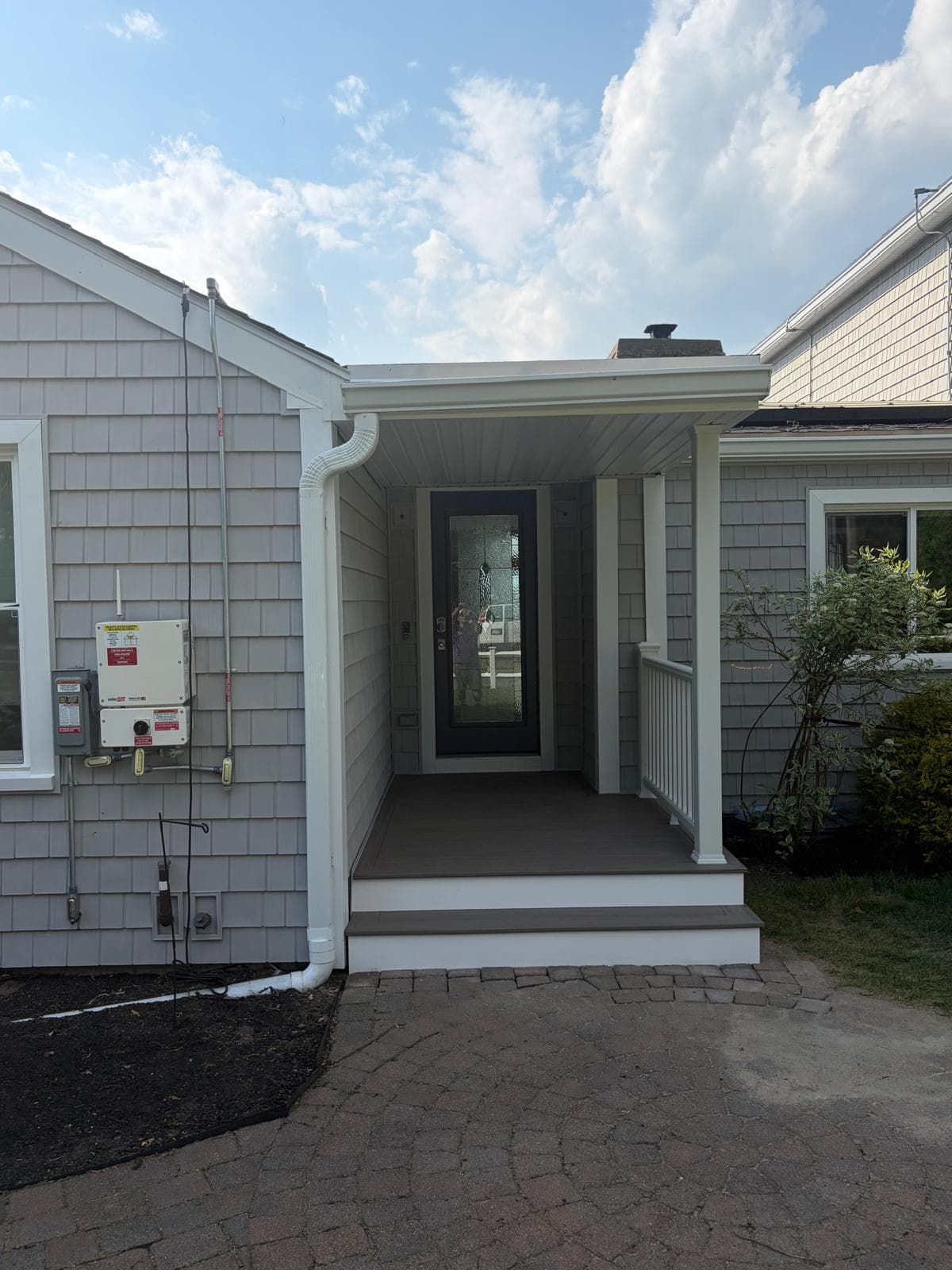 Front view of completed Webster MA covered porch addition — new entry door, matched cedar shake siding, composite floor