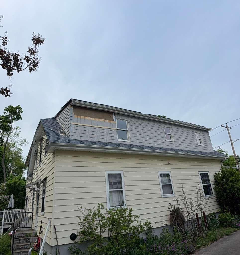 Warren RI two-story home with new gray cedar shake siding nearly complete on dormer — small finish patch remaining at top center